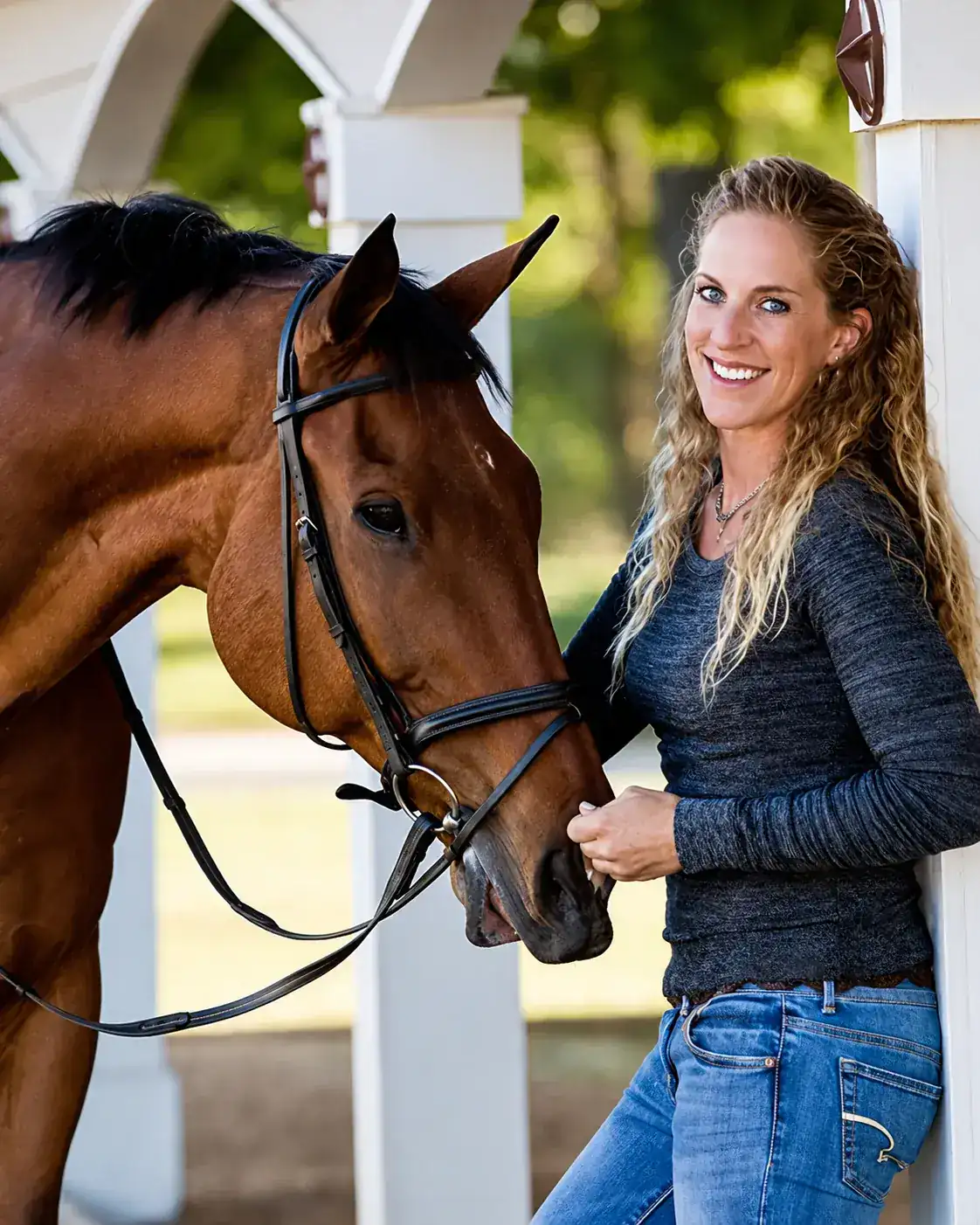 Laura de pie junto a un caballo alazán ensillado.